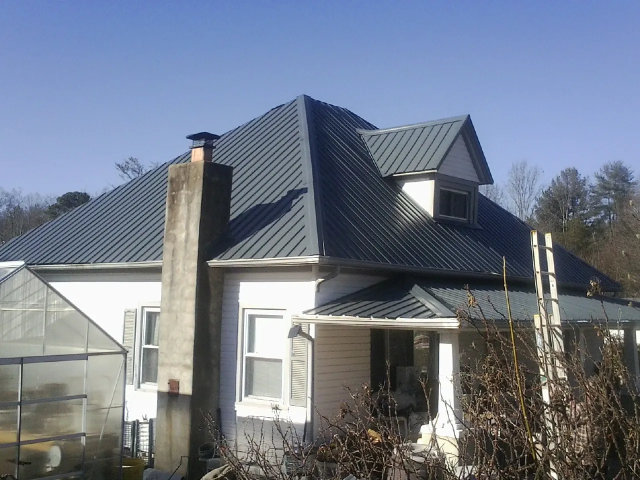 Dark blue standing seam metal roof on a white farmhouse with dormer — Slate & Tile Roof Repair by Roofing Brothers in Molina