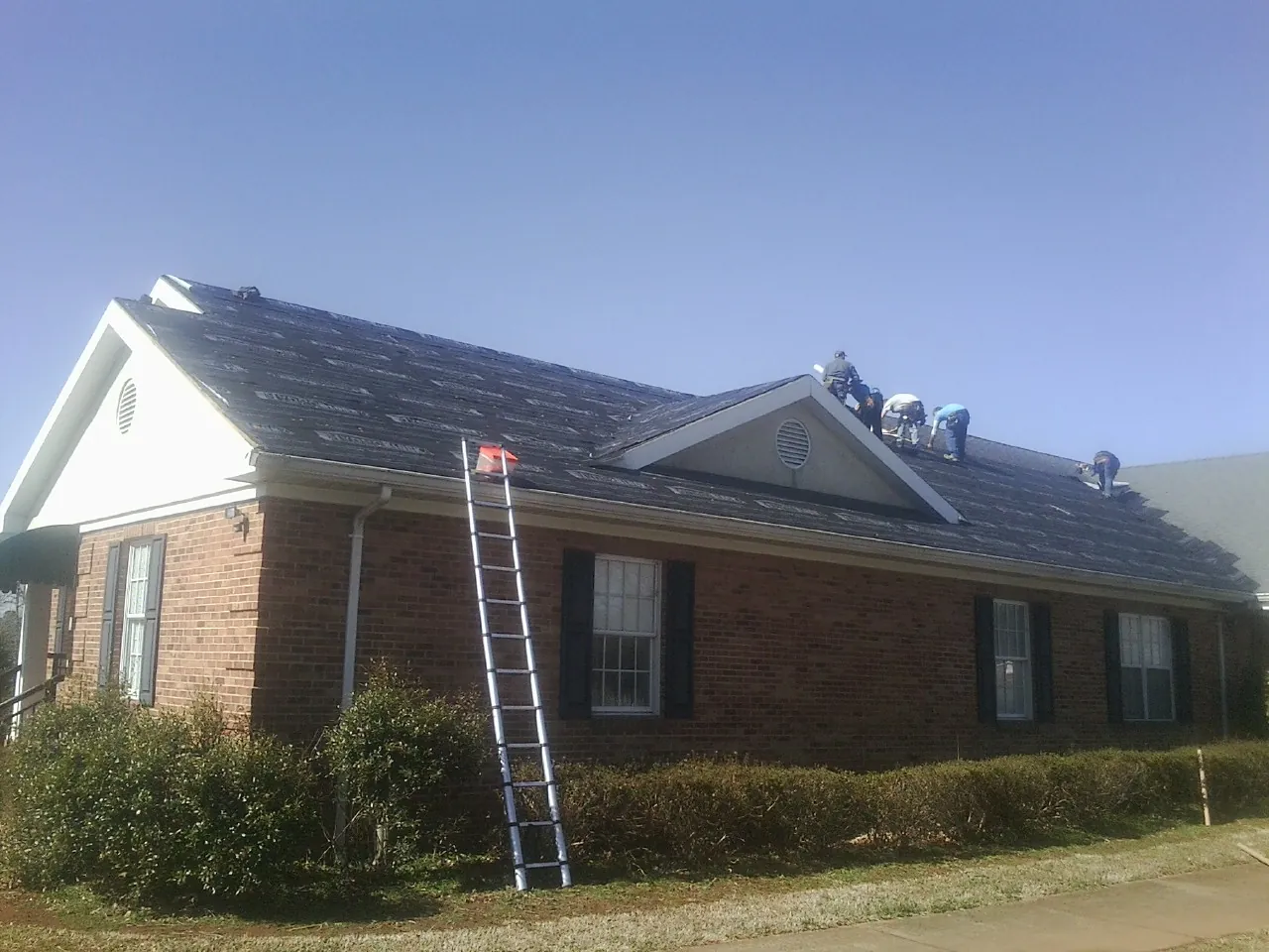 Crew tearing shingles off a brick ranch roof with a ladder set — Emergency Roof Repair work by our crew in Molina