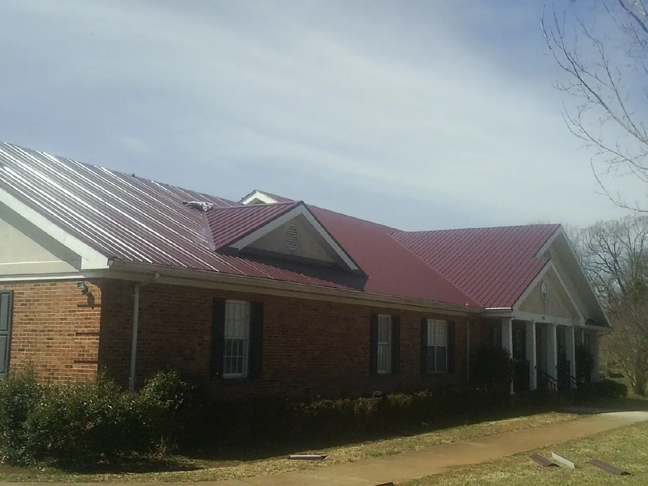 Red metal roof with gabled entries on a long brick building, from a Hail Damage Roof Repair job in Molina
