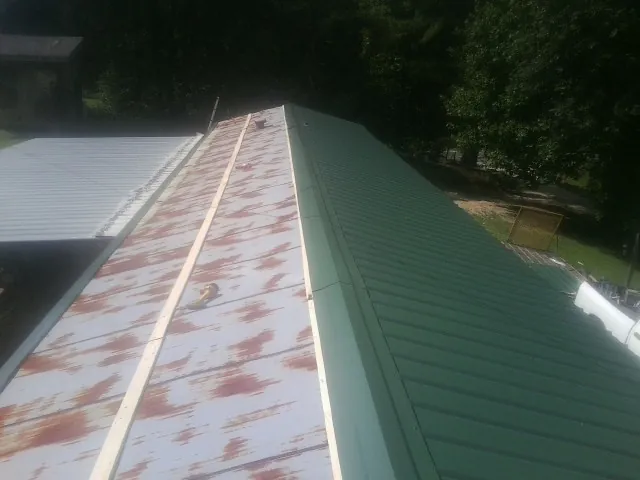 Old rusted panels beside newly installed green metal roofing — Wind Damage Roof Repair by Roofing Brothers in Molina