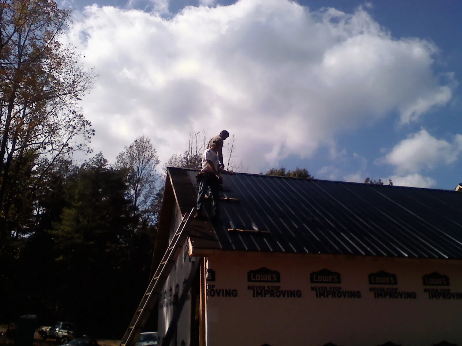 Roofer fastening dark metal panels high against a cloudy sky, from a Roof Inspection job in Molina