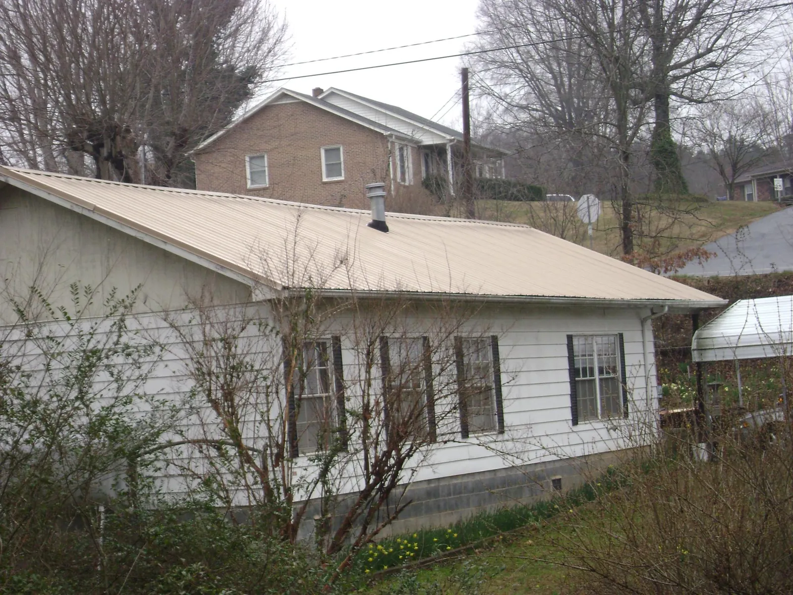 Tan metal roof on a white sided house set into a hillside — Commercial Roofing by Roofing Brothers in Molina
