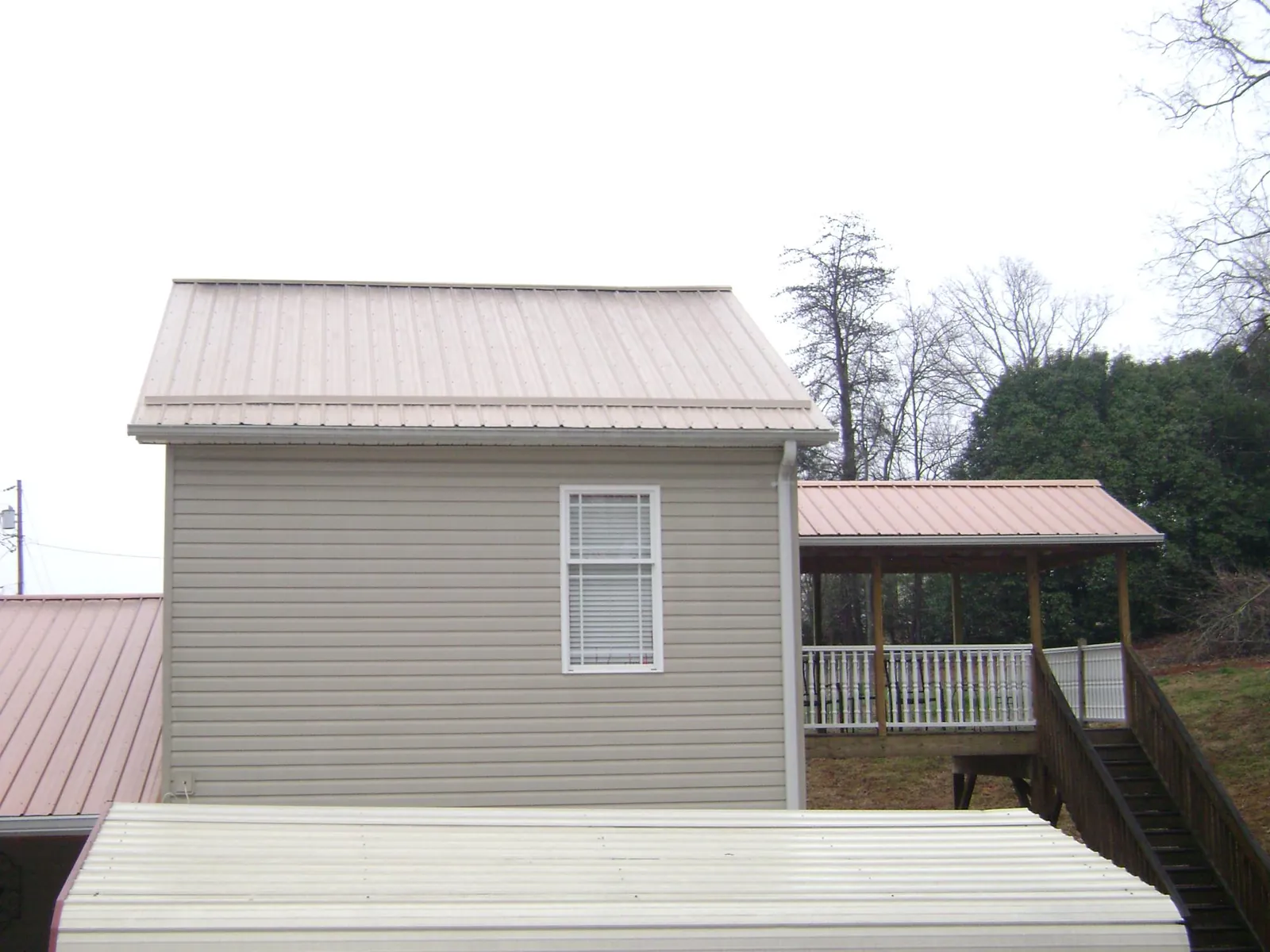 Tan metal roofs on a two story addition and attached porch, from a Roof Replacement job in Molina